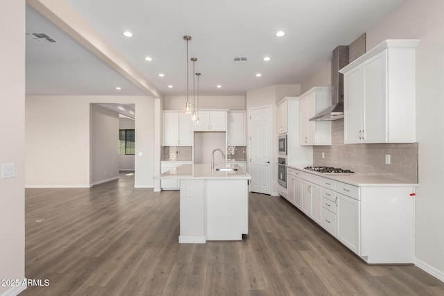 kitchen with white cabinetry, an island with sink, sink, hanging light fixtures, and wall chimney exhaust hood