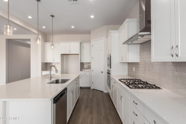 kitchen with appliances with stainless steel finishes, decorative light fixtures, sink, a kitchen island with sink, and wall chimney exhaust hood