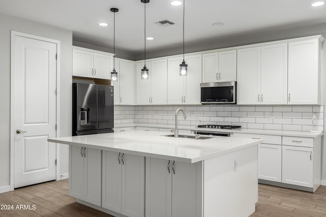 kitchen with an island with sink, appliances with stainless steel finishes, white cabinets, and decorative light fixtures