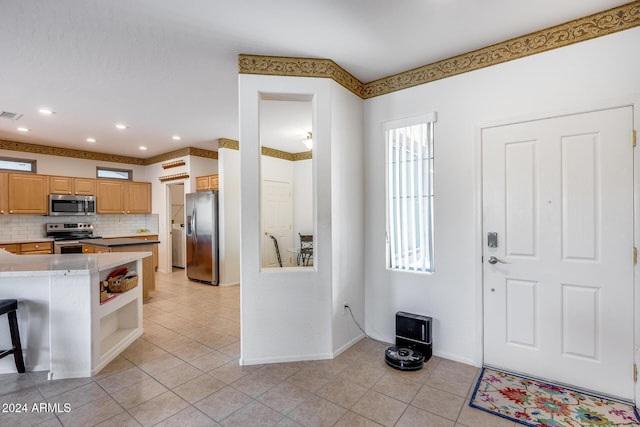 kitchen featuring a kitchen bar, appliances with stainless steel finishes, backsplash, light brown cabinetry, and light tile patterned flooring