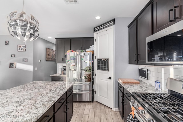 kitchen with light stone countertops, stainless steel appliances, tasteful backsplash, a notable chandelier, and decorative light fixtures