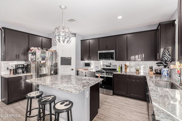 kitchen with sink, hanging light fixtures, a kitchen island, dark brown cabinetry, and stainless steel appliances