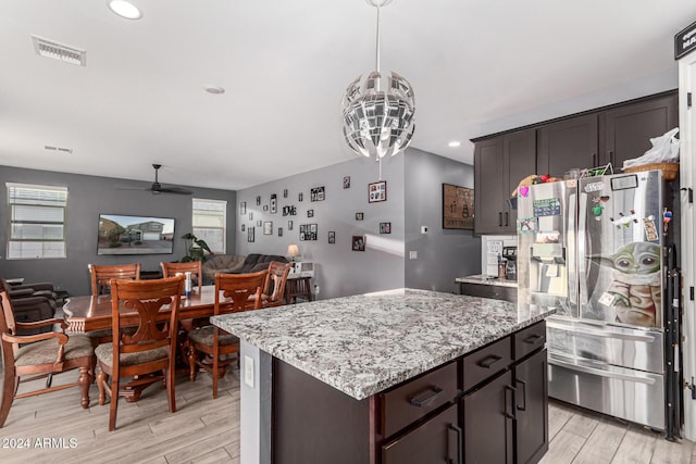 kitchen with ceiling fan, light stone counters, stainless steel refrigerator with ice dispenser, dark brown cabinets, and a kitchen island