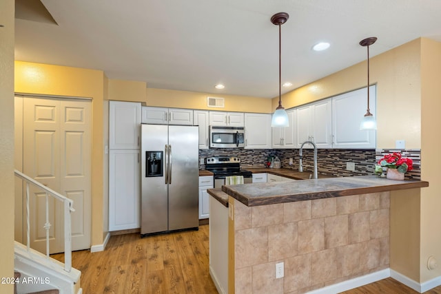 kitchen featuring light hardwood / wood-style flooring, kitchen peninsula, pendant lighting, white cabinets, and appliances with stainless steel finishes