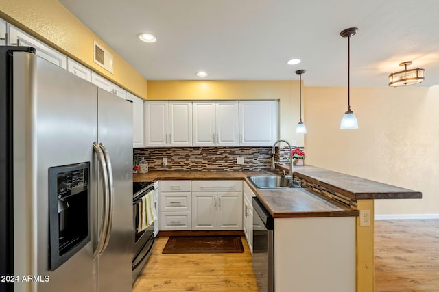 kitchen featuring pendant lighting, kitchen peninsula, light hardwood / wood-style flooring, white cabinetry, and stainless steel appliances