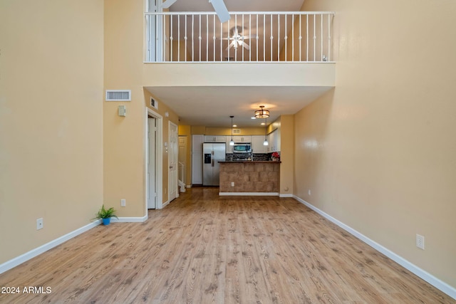 unfurnished living room featuring ceiling fan, light hardwood / wood-style floors, and a high ceiling