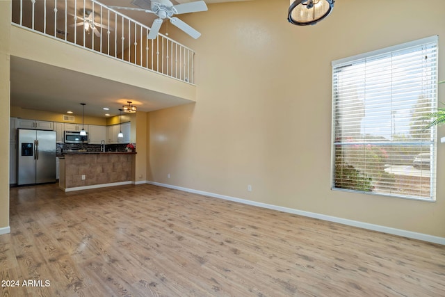 unfurnished living room with ceiling fan, sink, a high ceiling, and light wood-type flooring