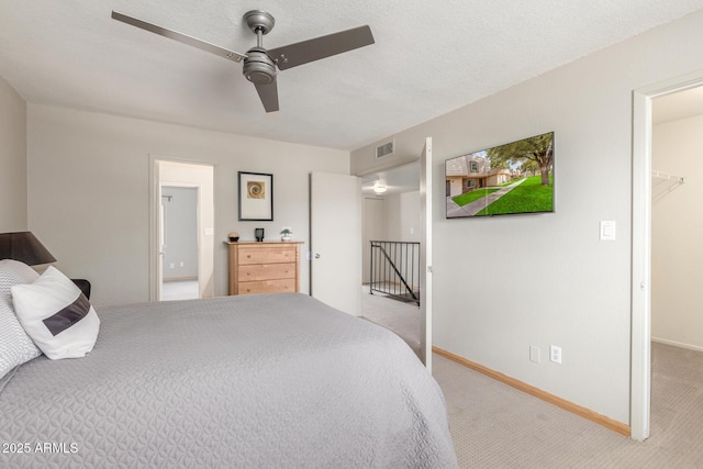 carpeted bedroom with a textured ceiling, a walk in closet, and ceiling fan