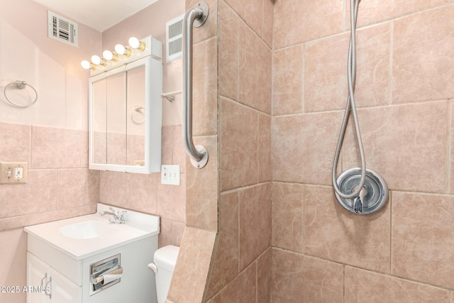 bathroom featuring vanity, a tile shower, tile walls, and toilet