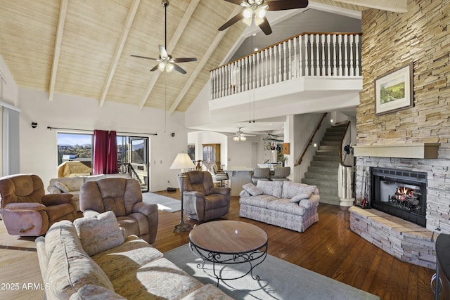 living room with beamed ceiling, wood-type flooring, high vaulted ceiling, and a stone fireplace