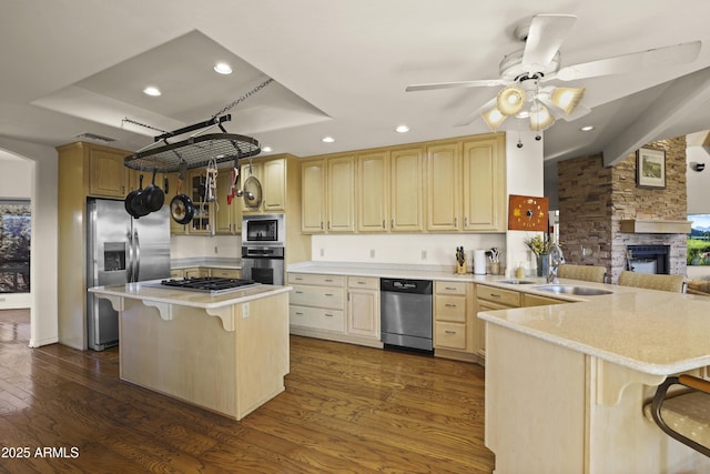 kitchen with a stone fireplace, dark hardwood / wood-style flooring, kitchen peninsula, a kitchen bar, and appliances with stainless steel finishes