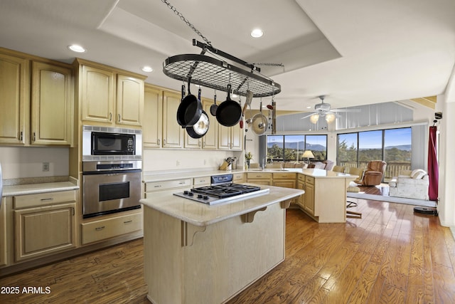 kitchen featuring kitchen peninsula, appliances with stainless steel finishes, a breakfast bar, hardwood / wood-style floors, and a kitchen island