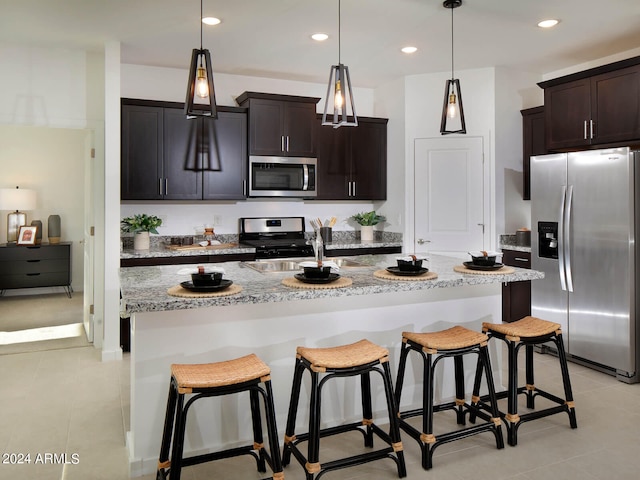 kitchen featuring hanging light fixtures, stainless steel appliances, dark brown cabinets, and a kitchen island with sink