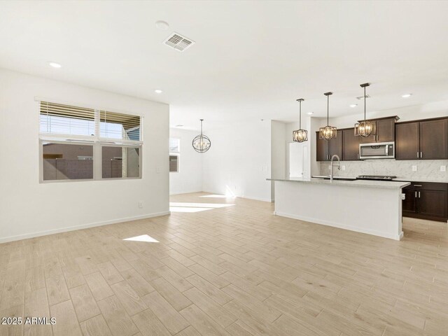 kitchen with pendant lighting, decorative backsplash, dark brown cabinets, and light wood-type flooring