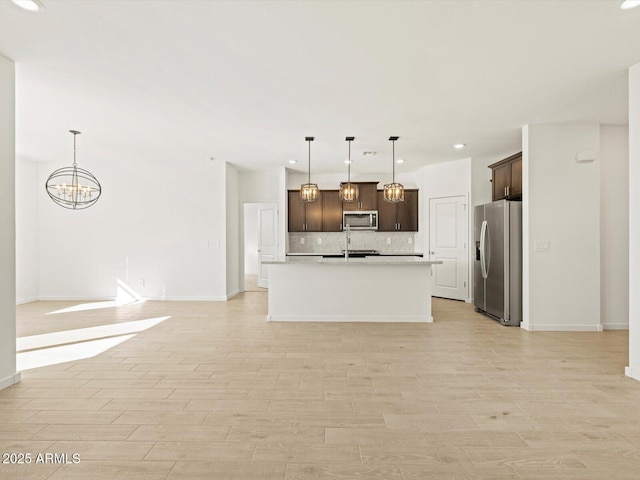 kitchen featuring dark brown cabinetry, tasteful backsplash, appliances with stainless steel finishes, pendant lighting, and a kitchen island with sink