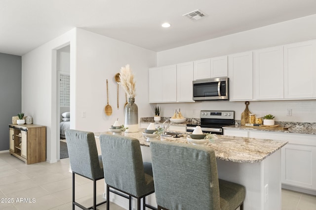 kitchen with light stone counters, stainless steel appliances, light tile patterned floors, visible vents, and a center island with sink