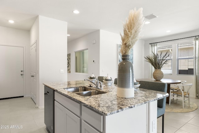 kitchen with light stone counters, a sink, dishwasher, an island with sink, and light tile patterned floors