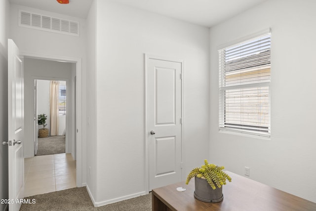 hallway featuring light tile patterned flooring, baseboards, visible vents, and light carpet