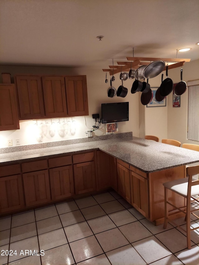 kitchen featuring a kitchen breakfast bar, light stone countertops, light tile patterned floors, and kitchen peninsula