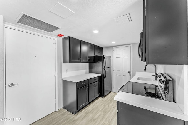 kitchen featuring sink, light hardwood / wood-style floors, a textured ceiling, and black appliances