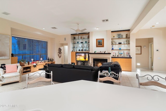 living room with light tile patterned floors, recessed lighting, visible vents, and a warm lit fireplace