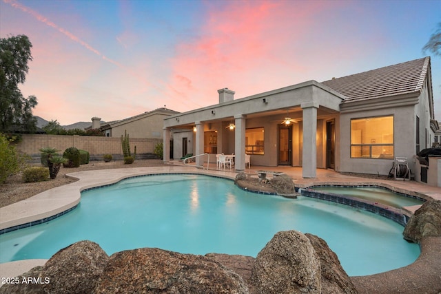 pool at dusk with a patio area, a pool with connected hot tub, ceiling fan, and fence