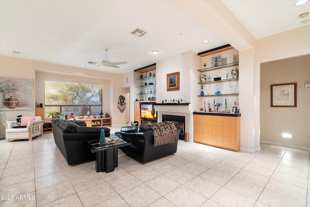 living area with built in shelves, baseboards, light tile patterned floors, a tile fireplace, and a ceiling fan