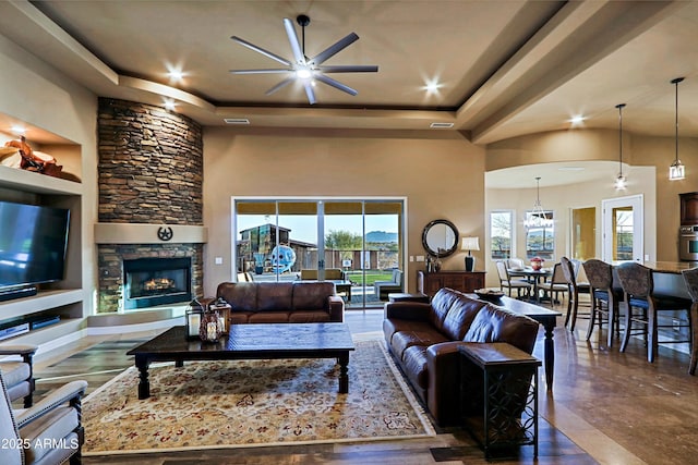 living area featuring a wealth of natural light, a raised ceiling, ceiling fan, and a fireplace