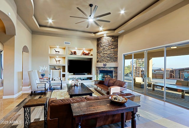 living area with visible vents, built in shelves, a ceiling fan, arched walkways, and a raised ceiling