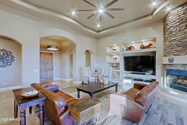 living room featuring visible vents, built in shelves, arched walkways, a fireplace, and ceiling fan