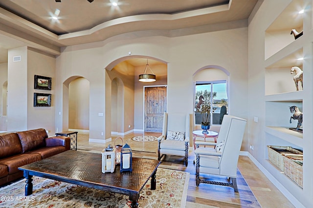 living area featuring a tray ceiling, built in features, baseboards, and arched walkways