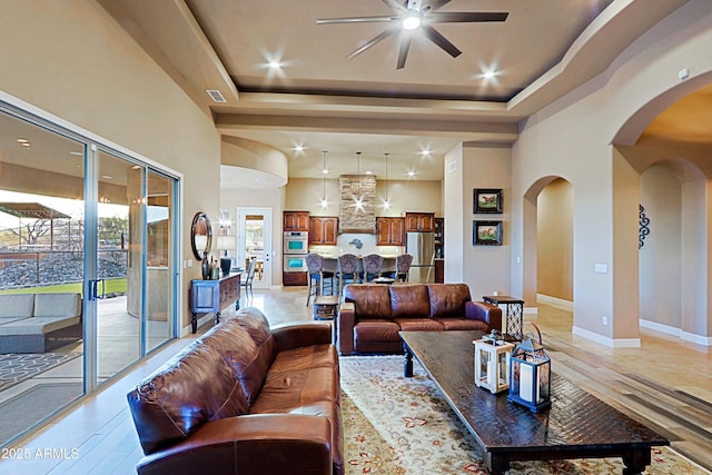 living room featuring visible vents, a tray ceiling, arched walkways, ceiling fan, and a towering ceiling