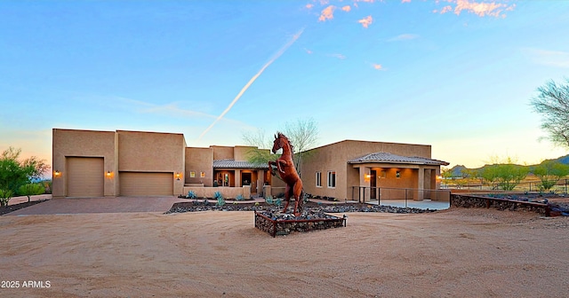 southwest-style home featuring stucco siding, driveway, a tile roof, fence, and an attached garage