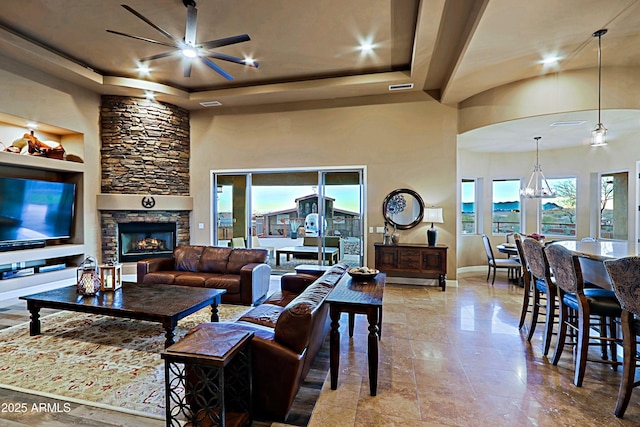 living room with visible vents, built in features, a fireplace, a raised ceiling, and a ceiling fan