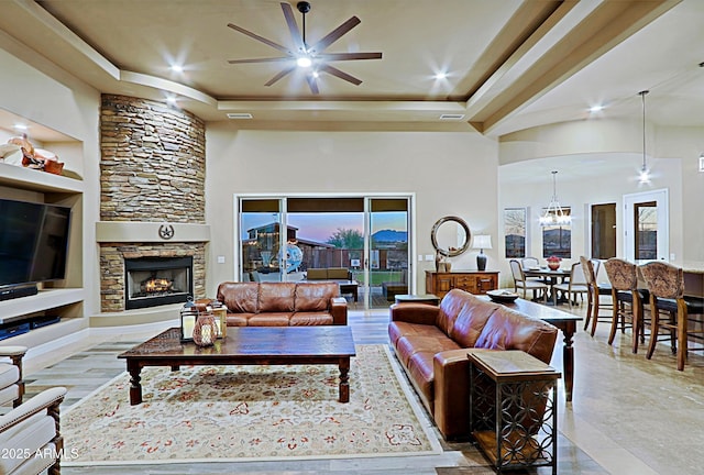 living room featuring visible vents, a tray ceiling, ceiling fan with notable chandelier, a fireplace, and a towering ceiling