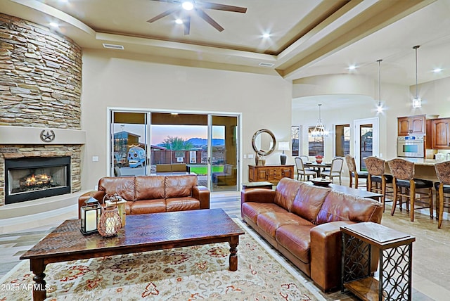 living room featuring visible vents, a fireplace, a towering ceiling, a raised ceiling, and ceiling fan with notable chandelier