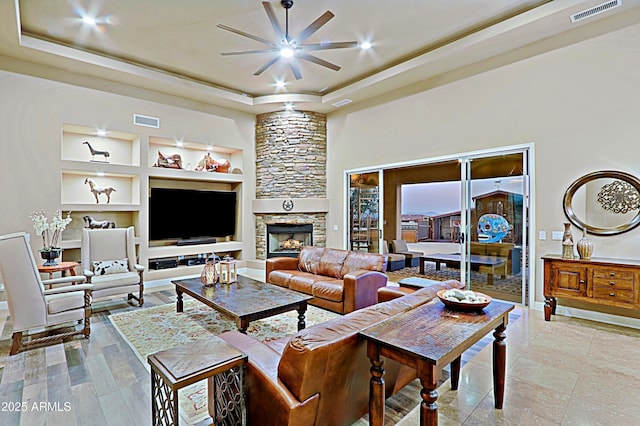 living area with a raised ceiling, built in features, visible vents, and ceiling fan