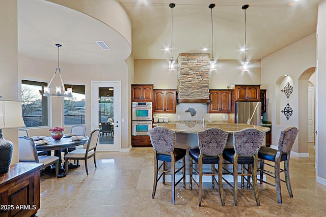 kitchen with a notable chandelier, pendant lighting, light stone counters, arched walkways, and appliances with stainless steel finishes