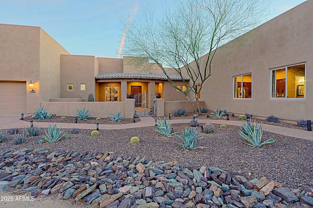 adobe home featuring a fenced front yard, stucco siding, a tiled roof, and a garage