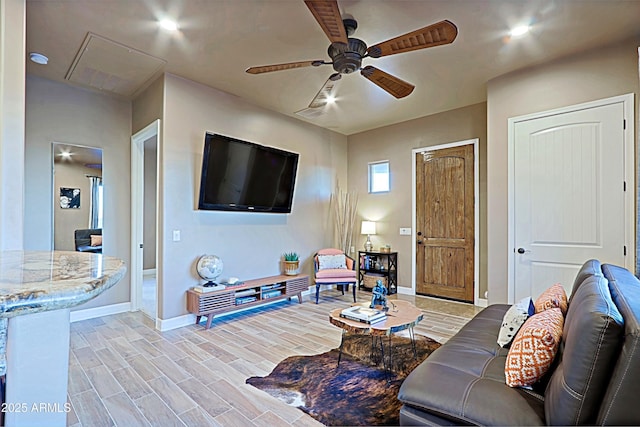 living room with attic access, a ceiling fan, light wood-style floors, and baseboards