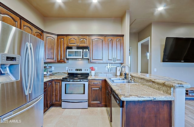 kitchen featuring a sink, a peninsula, light stone counters, and stainless steel appliances