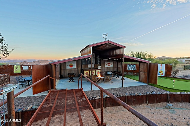 back of property at dusk featuring exterior fireplace, a patio, and fence