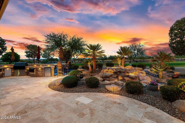 patio terrace at dusk featuring area for grilling and exterior kitchen