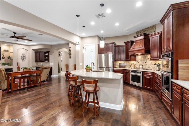 kitchen featuring premium range hood, pendant lighting, sink, a kitchen island with sink, and stainless steel appliances