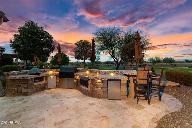 patio terrace at dusk featuring area for grilling and an outdoor kitchen