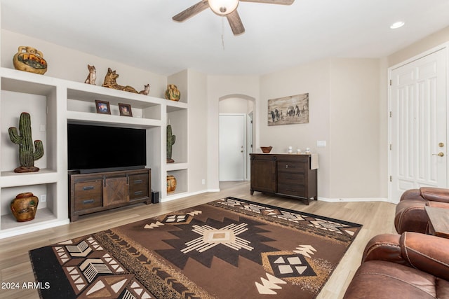 living room featuring built in shelves, light hardwood / wood-style floors, and ceiling fan