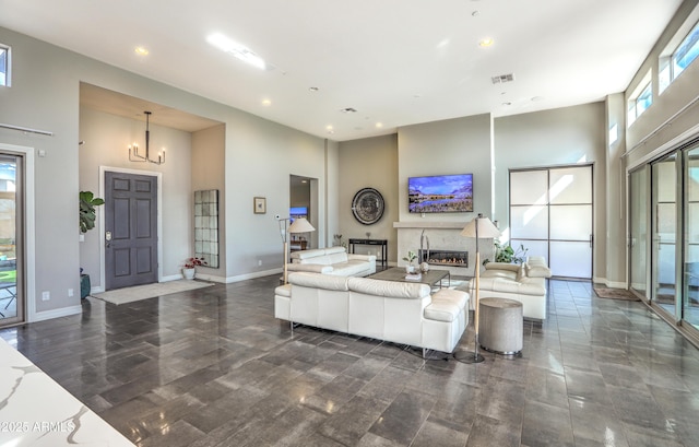 living room with baseboards, visible vents, a glass covered fireplace, a towering ceiling, and a chandelier