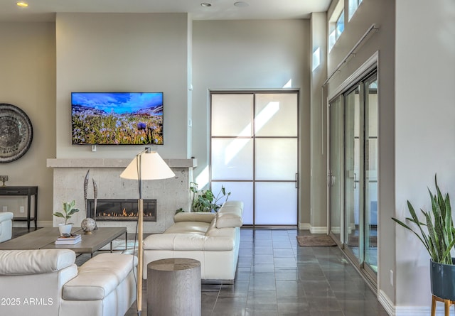 tiled living room with a high ceiling, baseboards, and a glass covered fireplace