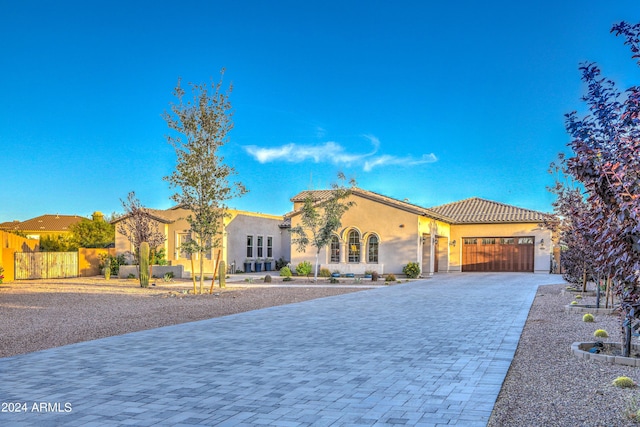 mediterranean / spanish house with a garage, fence, a tiled roof, decorative driveway, and stucco siding