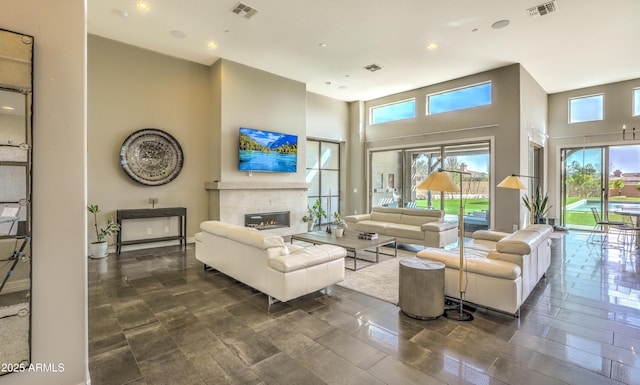 living area featuring a glass covered fireplace, visible vents, and a high ceiling